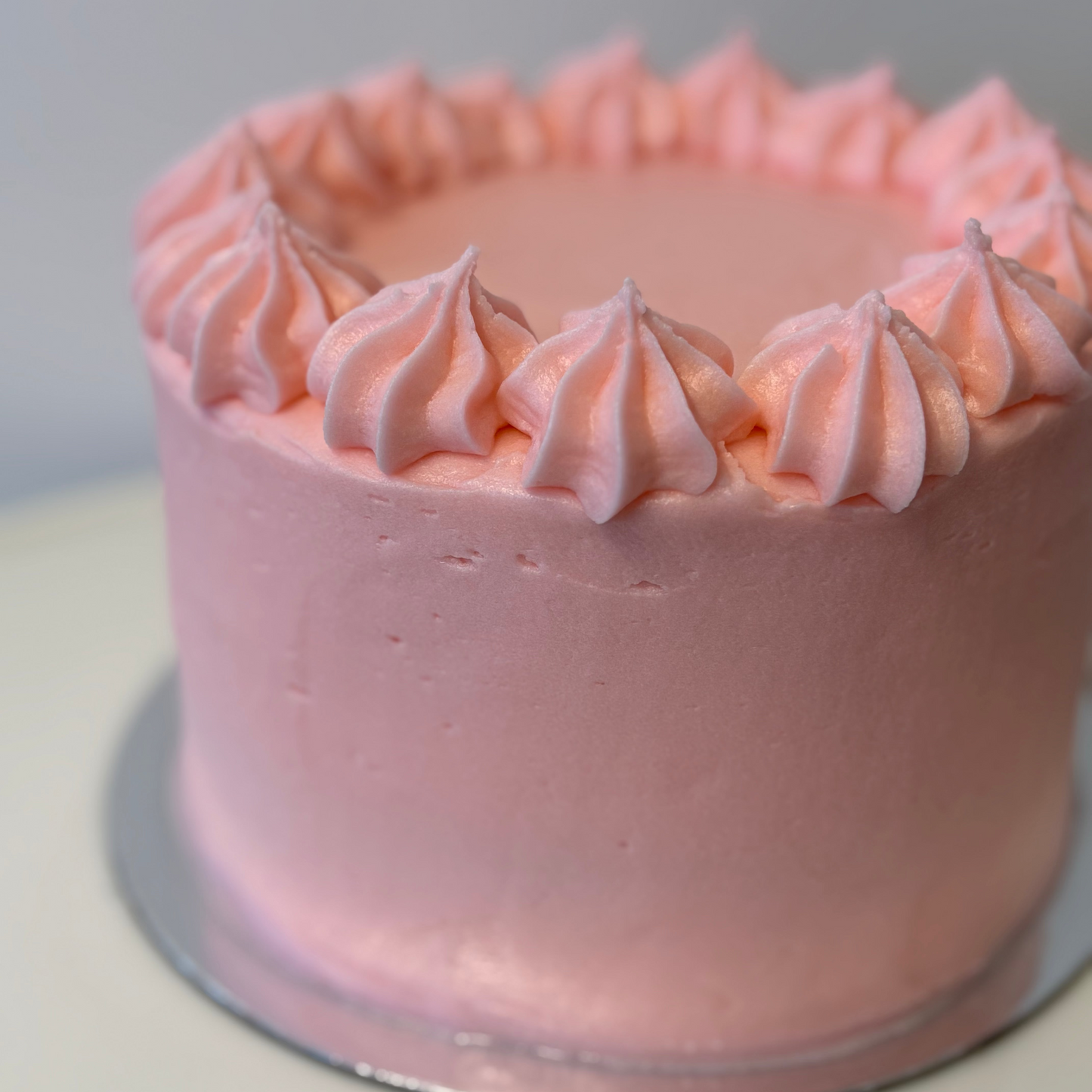 Pink frosted cake on a white surface with a light gray background