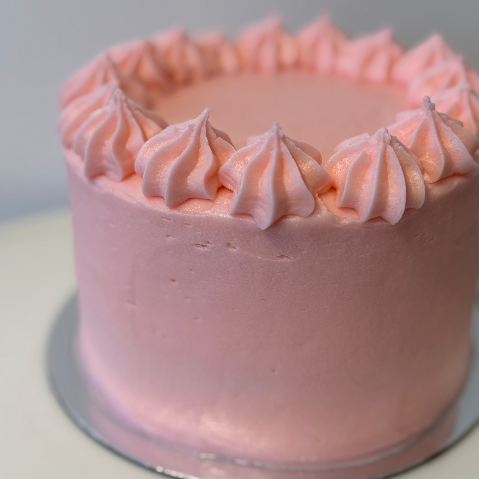 Pink frosted cake on a white surface with a light gray background